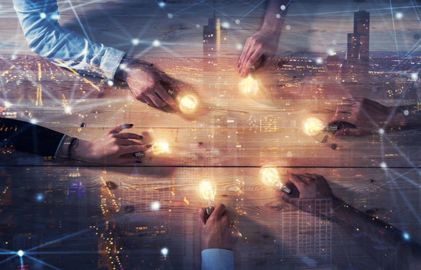 hands holding light bulbs with a city scape image in background